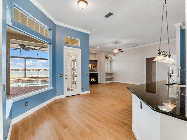 kitchen with sink, dark stone countertops, crown molding, decorative light fixtures, and light wood-type flooring