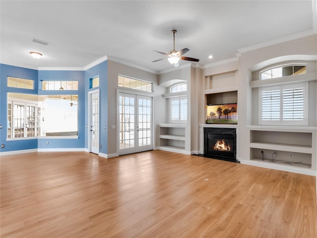 unfurnished living room featuring built in shelves, a healthy amount of sunlight, light wood-type flooring, and french doors