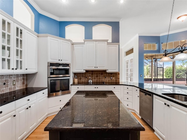 kitchen with dark stone countertops, light wood-type flooring, a kitchen island, white cabinetry, and stainless steel appliances