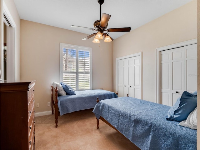 bedroom featuring ceiling fan, light colored carpet, and two closets