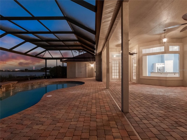 pool at dusk featuring glass enclosure, ceiling fan, and a patio area