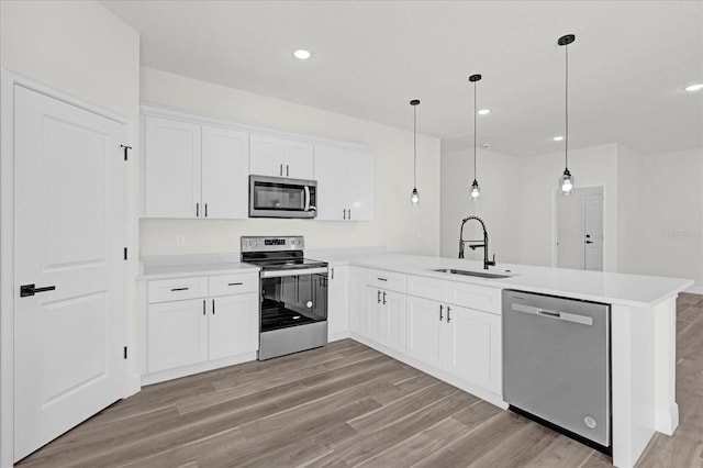 kitchen with sink, white cabinets, kitchen peninsula, pendant lighting, and appliances with stainless steel finishes