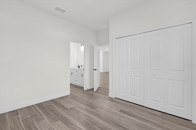 unfurnished bedroom with ensuite bath, a closet, and light wood-type flooring