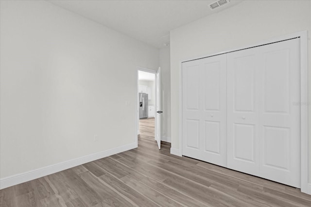 unfurnished bedroom with stainless steel refrigerator with ice dispenser, a closet, and light hardwood / wood-style floors