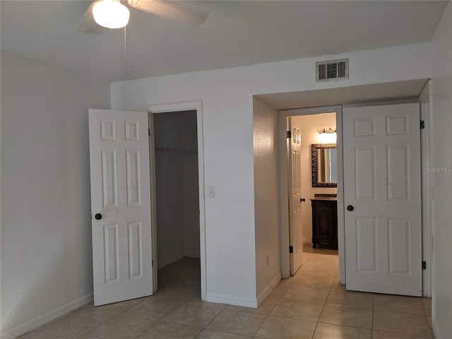 unfurnished bedroom with ensuite bath, ceiling fan, a walk in closet, a closet, and light tile patterned floors