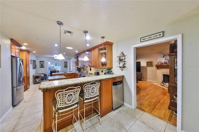 kitchen with light stone countertops, light tile patterned floors, kitchen peninsula, and stainless steel refrigerator