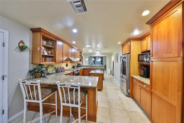 kitchen with light stone counters, kitchen peninsula, a textured ceiling, a kitchen bar, and appliances with stainless steel finishes