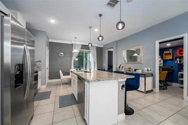 kitchen with pendant lighting, a kitchen island with sink, sink, appliances with stainless steel finishes, and white cabinetry