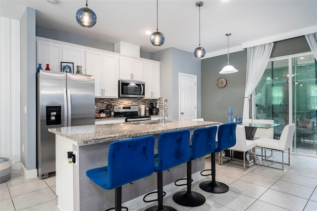 kitchen with white cabinets, stainless steel appliances, hanging light fixtures, and a center island with sink