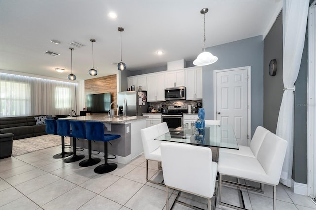 kitchen featuring appliances with stainless steel finishes, a breakfast bar, pendant lighting, white cabinetry, and an island with sink