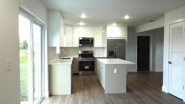 kitchen with sink, a kitchen island, appliances with stainless steel finishes, white cabinets, and hardwood / wood-style flooring