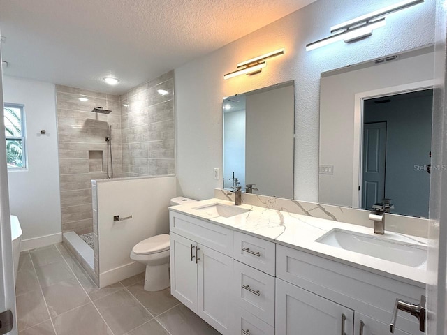 bathroom featuring vanity, tile patterned flooring, toilet, a textured ceiling, and a tile shower