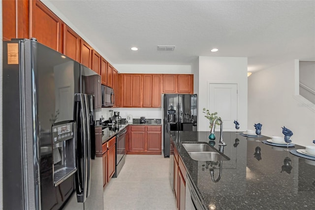 kitchen featuring sink, dark stone countertops, light tile patterned floors, a textured ceiling, and appliances with stainless steel finishes