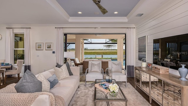 living room featuring wood-type flooring, a water view, ornamental molding, and a tray ceiling