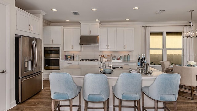 851 Arbor Green Trl, Saint Cloud, FL 34771 - kitchen featuring stainless steel appliances, under cabinet range hood, light countertops, a kitchen breakfast bar, and white cabinetry