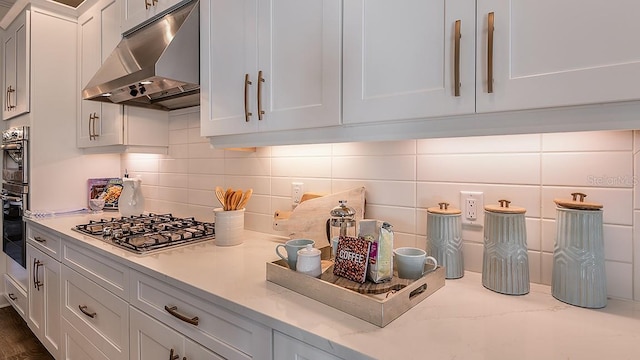 kitchen featuring backsplash, light stone counters, white cabinets, oven, and stainless steel gas stovetop