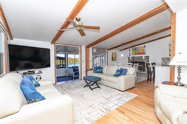 living room with wood-type flooring, lofted ceiling with beams, a textured ceiling, ceiling fan, and a fireplace