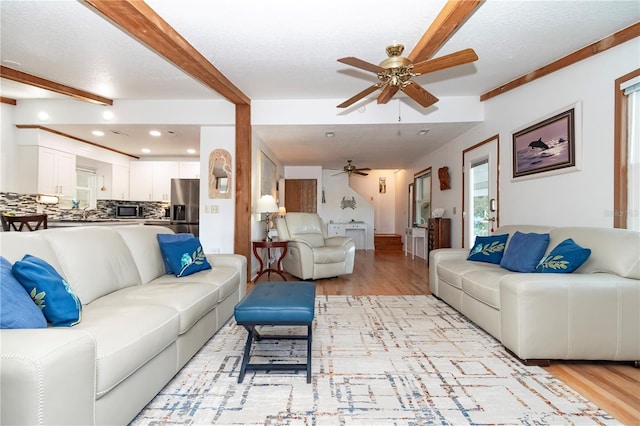 living room featuring beamed ceiling, ceiling fan, light hardwood / wood-style flooring, and a textured ceiling