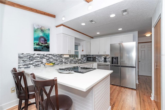 kitchen with appliances with stainless steel finishes, white cabinetry, a textured ceiling, a kitchen bar, and kitchen peninsula