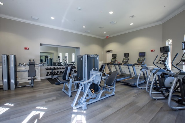 exercise room featuring a towering ceiling, ornamental molding, and hardwood / wood-style flooring