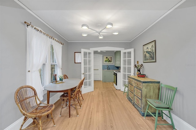 dining room featuring an inviting chandelier, ornamental molding, light hardwood / wood-style flooring, and french doors