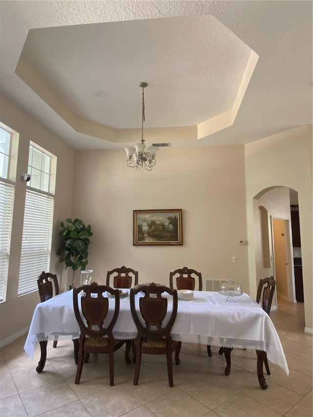 tiled dining area featuring a raised ceiling, a textured ceiling, and a chandelier