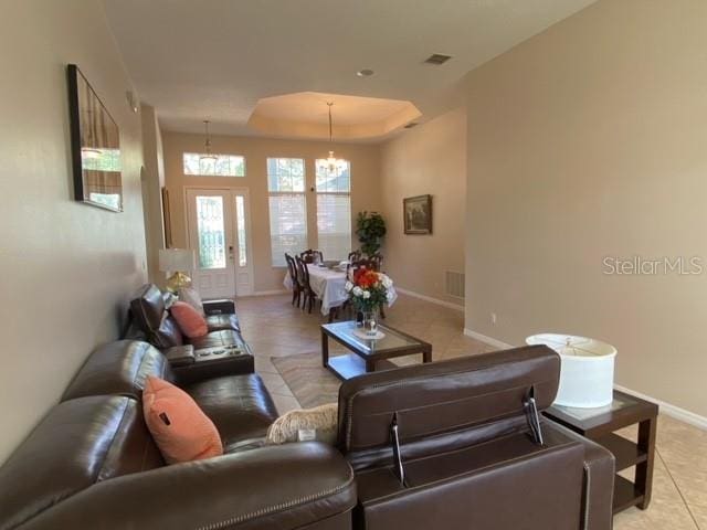 living room featuring a tray ceiling, french doors, light tile patterned floors, and an inviting chandelier