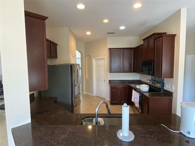 kitchen featuring sink, dark stone counters, a textured ceiling, light tile patterned floors, and appliances with stainless steel finishes