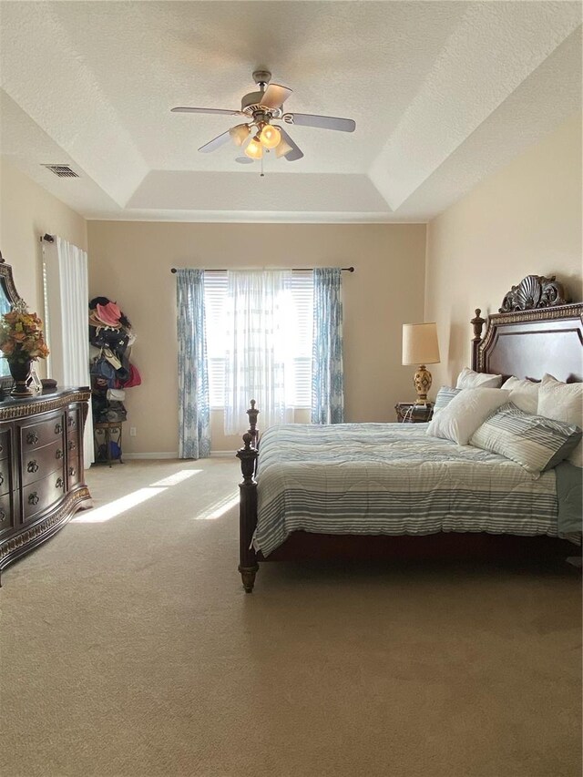 bedroom featuring a textured ceiling, carpet floors, a tray ceiling, and ceiling fan