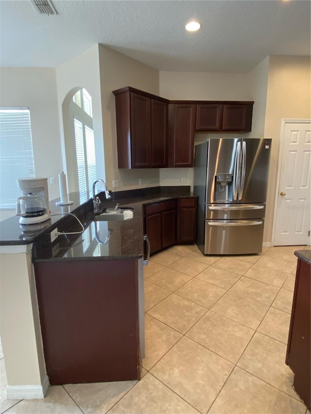 kitchen with kitchen peninsula, stainless steel refrigerator with ice dispenser, dark stone counters, sink, and light tile patterned floors