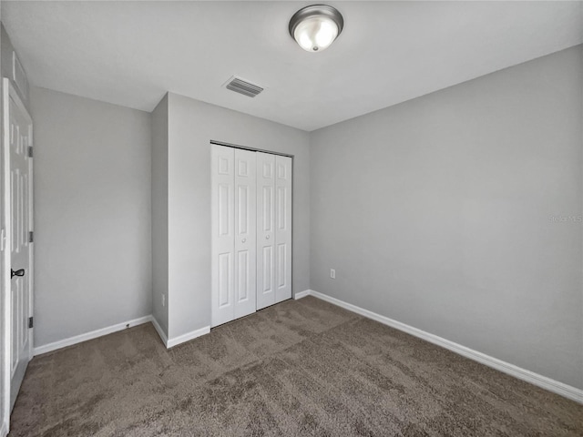 unfurnished bedroom with dark colored carpet and a closet