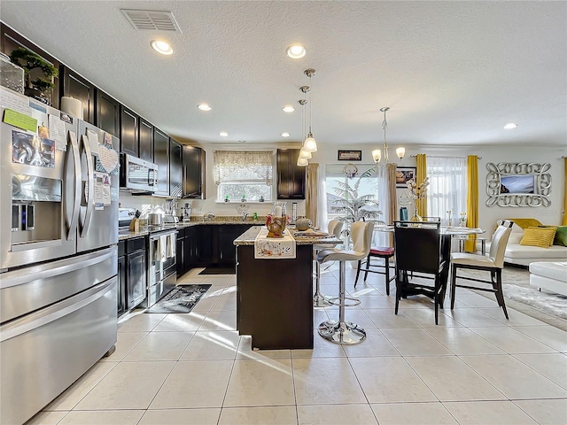 kitchen with a breakfast bar area, light tile patterned floors, decorative light fixtures, a kitchen island, and stainless steel appliances