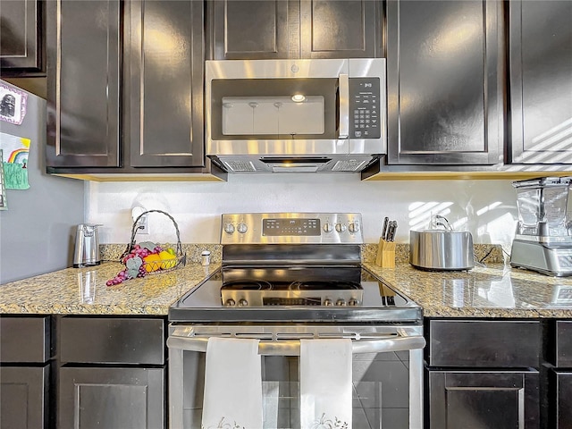 kitchen featuring dark brown cabinetry, light stone countertops, and appliances with stainless steel finishes