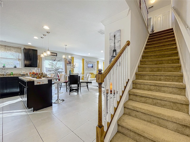 staircase with a textured ceiling, tile patterned floors, crown molding, and a notable chandelier