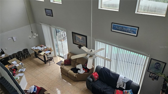 living room with light tile patterned floors, a towering ceiling, and ceiling fan with notable chandelier