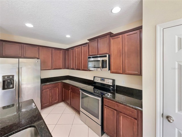 kitchen with sink, stainless steel appliances, dark stone counters, a textured ceiling, and light tile patterned floors