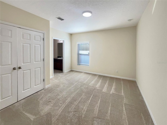 unfurnished bedroom featuring ensuite bathroom, light colored carpet, a textured ceiling, and a closet