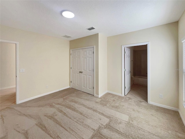 unfurnished bedroom with connected bathroom, a closet, light colored carpet, and a textured ceiling