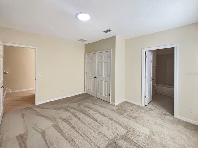 unfurnished bedroom with light carpet, a textured ceiling, ensuite bathroom, and a closet