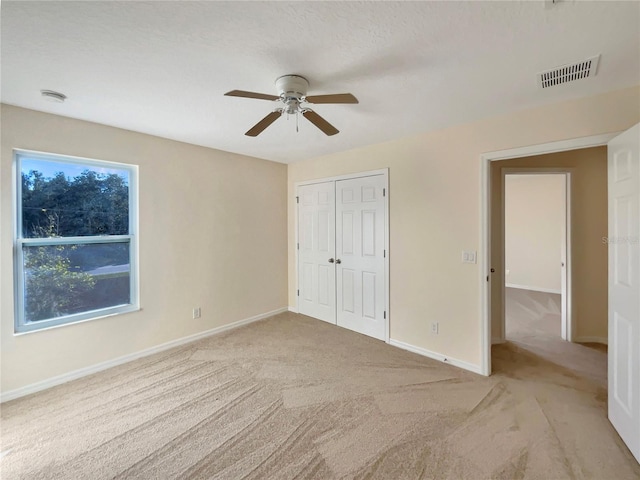 unfurnished bedroom featuring light carpet, a textured ceiling, a closet, and ceiling fan