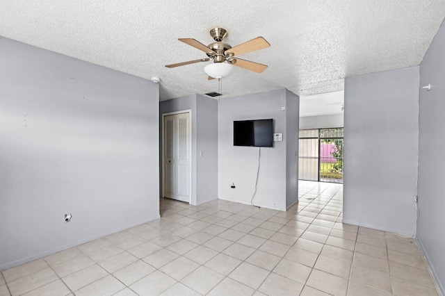 empty room featuring ceiling fan, light tile patterned floors, and a textured ceiling