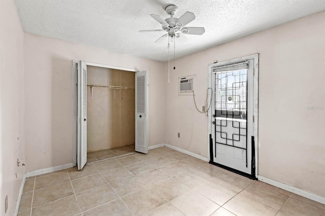 unfurnished bedroom featuring ceiling fan, light tile patterned floors, a textured ceiling, a wall unit AC, and a closet