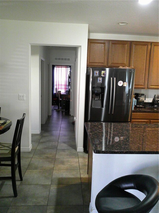 kitchen featuring stainless steel refrigerator with ice dispenser, dark tile patterned flooring, and dark stone counters