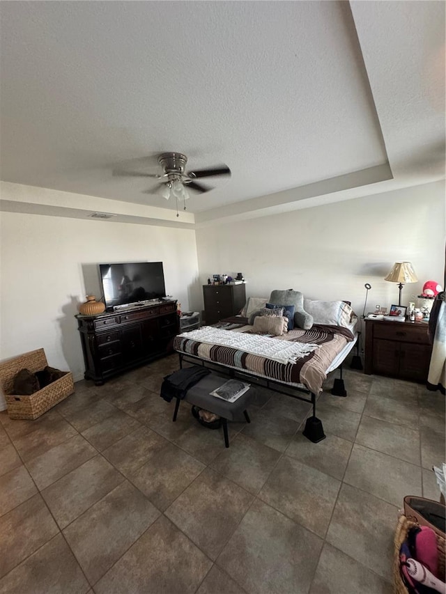 bedroom featuring a tray ceiling, ceiling fan, and a textured ceiling