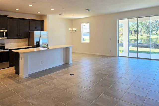 kitchen with backsplash, stainless steel appliances, sink, a center island with sink, and an inviting chandelier