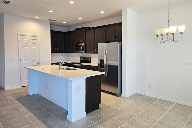 kitchen with stainless steel appliances, a kitchen island with sink, sink, a notable chandelier, and light tile patterned flooring