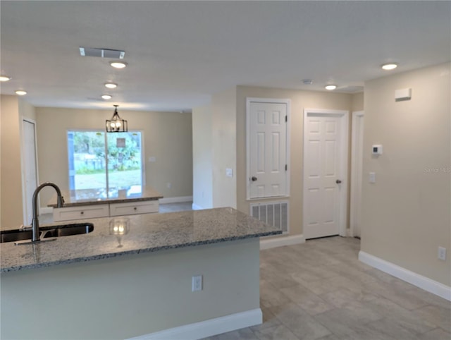 kitchen with light stone countertops, sink, an inviting chandelier, pendant lighting, and white cabinets