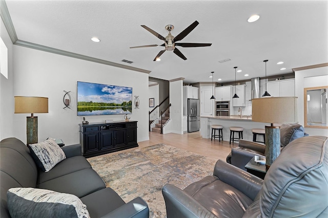 living area featuring ceiling fan, recessed lighting, visible vents, ornamental molding, and stairway