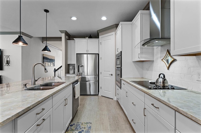 kitchen featuring white cabinets, wall chimney exhaust hood, light stone counters, stainless steel appliances, and a sink