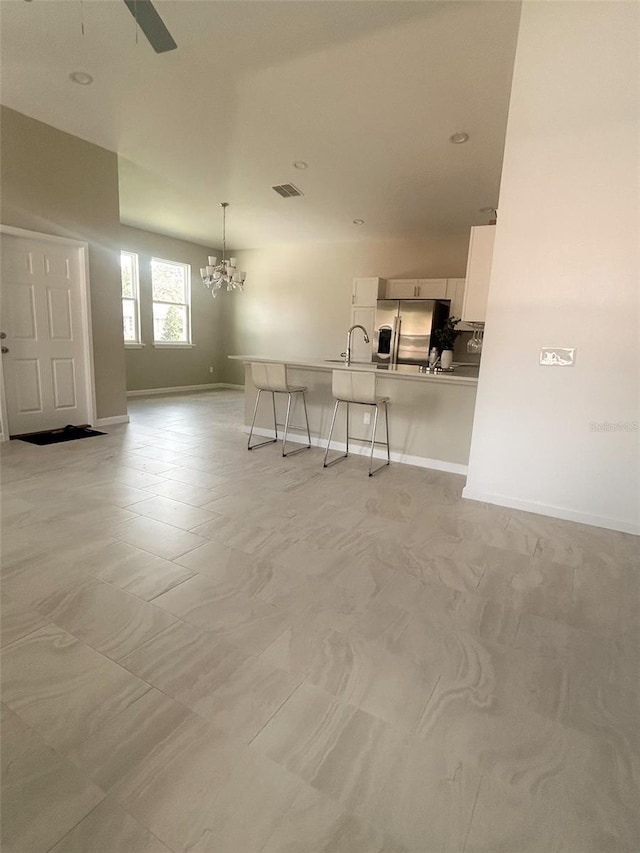 unfurnished living room featuring ceiling fan with notable chandelier, a sink, visible vents, and baseboards